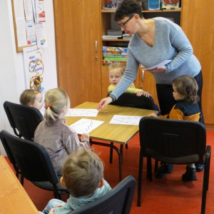 Bibliotekarka rozdaje przedszkolakom kolorowanki.