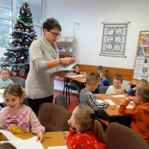 Bibliotekarka rozdaje dzieciom kartki z szablonem maski karnawałowej.