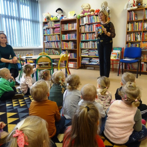 Bibliotekarka pokazuje przedszkolakom książkę z materiału.