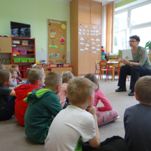 Przedszkolaki słuchają opowiadania czytanego przez bibliotekarkę.