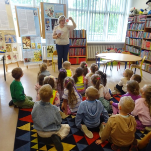 Bibliotekarka pokazuje dzieciom karteczkę z uśmiechniętą buzią