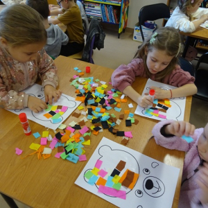 Przedszkolaki przyklejają bibułę na misiach