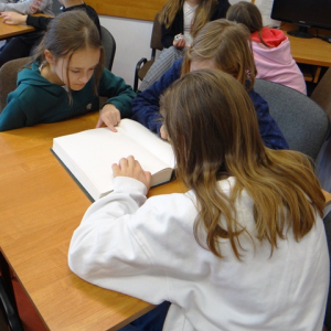 Uczniowie oglądają i dotykają książki dla osób niewidomych