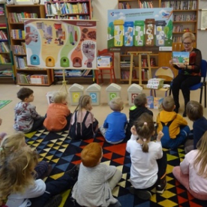 Bibliotekarka pokazuje przedszkolakom obrazki dotyczące segregacji śmieci.