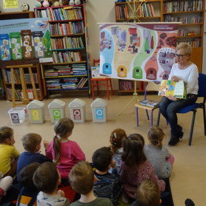 Bibliotekarka pokazuje przedszkolakom ilustracje z książki o śmieciach. 