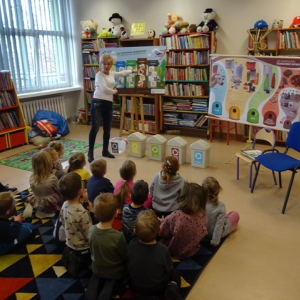 Bibliotekarka wyjaśnia przedszkolakom, jakie są rodzaje koszy do segregowania odpadów i co należy do nich wrzucać.